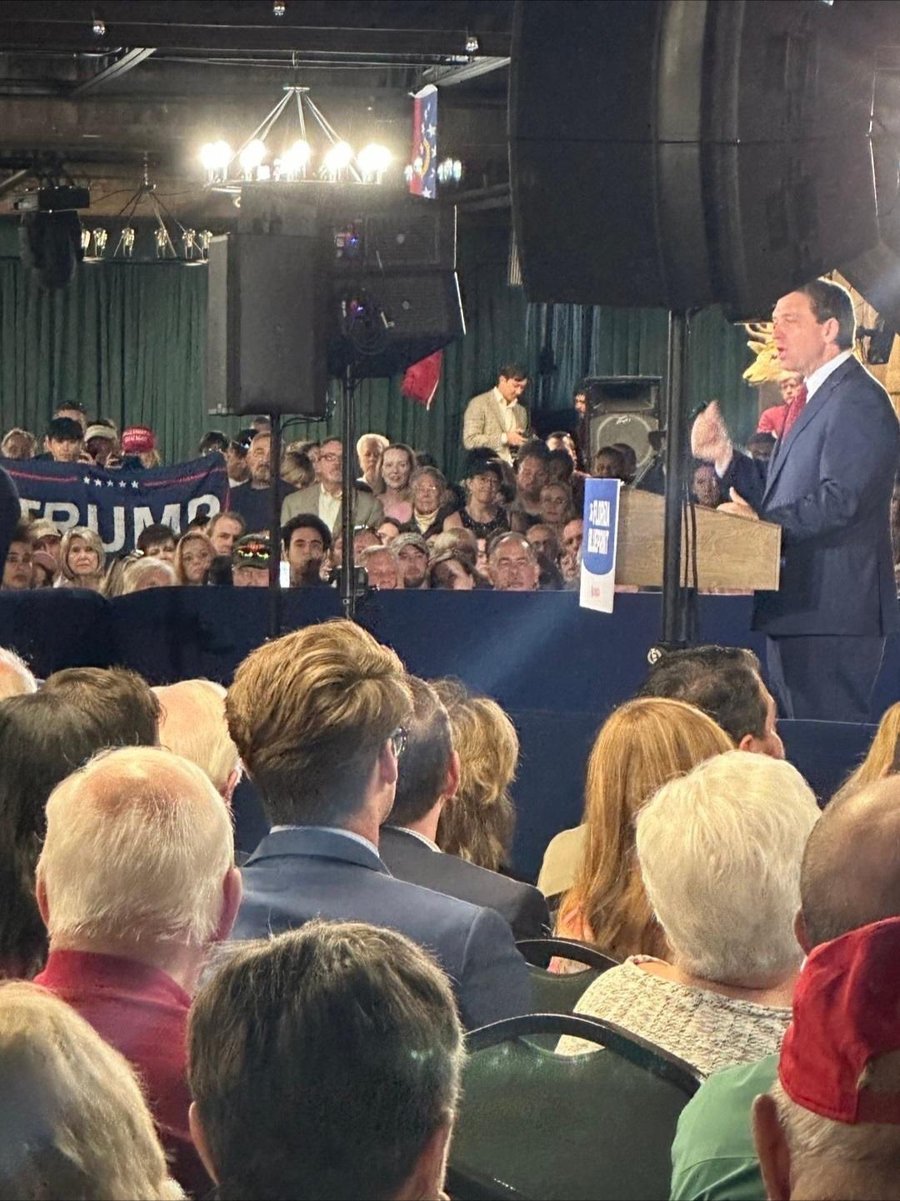 Ron DeSantis speaking at the Georgia event, with a Trump flag raised in the crowd